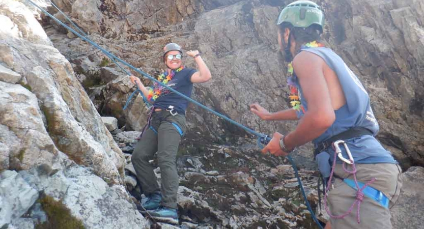 two gap year students preparing to rock climb go to high five one another on an outward bound outdoor educator course